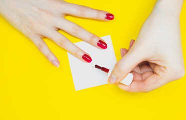 Woman applies red nail polish on the yellow background..Girl making a manicure. Salon procedures at home. Beautiful hands and nails. Close up, macro photo. Colorful and creative.