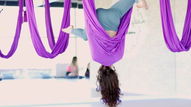 Young beautiful woman practice in stretching swing. Aerial flying yoga exercises practice in purple hammock in fitness club.