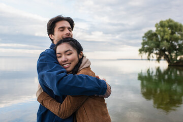Man embracing asian girlfriend near lake
