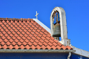 View of a cross and a church and a bell on a clear day.