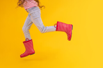 Girl with red rubber boots for rain over yellow background