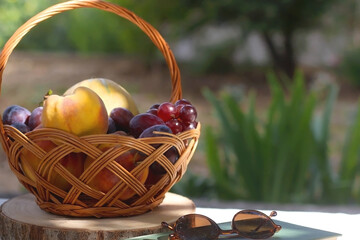 Vintage basket full of various fruit, hardback book and retro sunglasses on picnic basket....