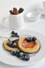 Cottage cheese pancakes with honey and blueberries on the white plate. Soft focus.
