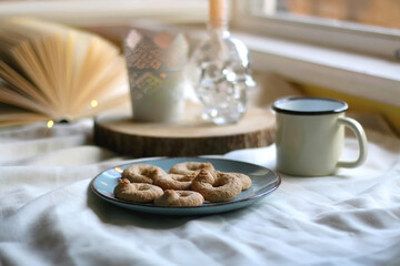 Plate with cookies, open book, lit candles and fairy lights. Hygge at home. Selective focus.