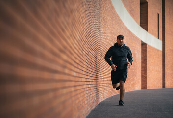 Asia man wearing jacket sportswear running on the road under the building. Young man jogging for...