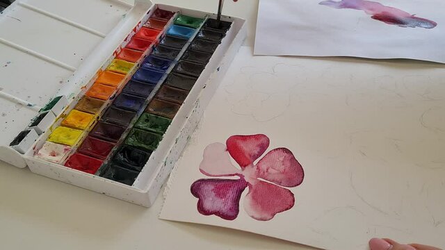 Artists hand paints a purple flower with watercolors close up