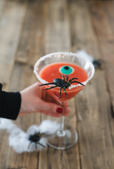 Woman hand holding a cocktail for Halloween day on a rustic wooden table. Copy space. Vertical photo.