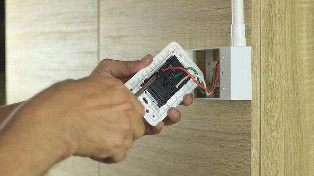 Electrician is using a screwdriver to remove the wires to the electrical plug on a wooden wall.