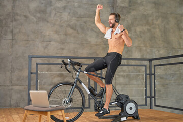 Fototapeta na wymiar Excited joyful man having stationary bike workout at home