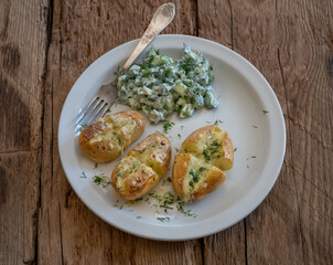 Baked potatoes with cheese and cucumber salad with sour cream on white plate.