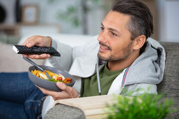 young man on the phone enjoying salad while watching tv