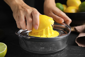 Woman squeezing lemon juice at black table, closeup