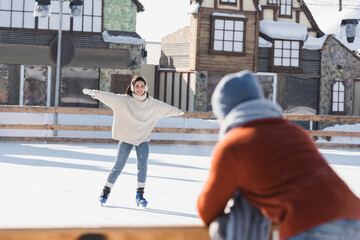 smiling woman skating on ice rink and looking at blurred boyfriend on foreground