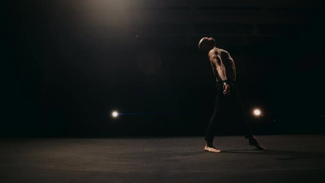 A ballet male dancer is performing choreography on classic theater stage. Choreographer is practicing dance moves. Acrobatic elements of contemporary dance. Performance concept. 4k footage.