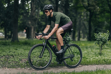Fototapeta na wymiar Male athlete in sport clothes riding bike at summer park