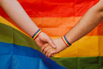Young gay couple with rainbow flag holding hands together during pride parade