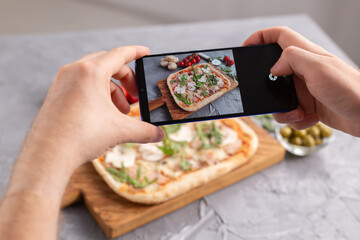 Chef takes pictures of the cooked of italian pizza with parma ham on smartphone. Photographing food and social networks concept.
