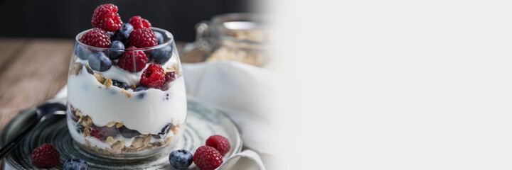Granola parfait with berries and yogurt with a copy space.  Parfait with granola , raspberries and blueberries on a white background with copy space. Granola in a glass .  Food banner with granola 