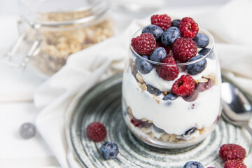 Granola parfait with berries and yogurt with a copy space.  Parfait with granola , raspberries and blueberries on a white background with copy space. Granola in a glass . 
