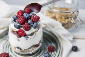 Granola parfait with berries and yogurt with a copy space.  Parfait with granola , raspberries and blueberries on a white background with copy space. Granola in a glass . 