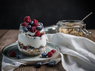 Granola parfait with berries and yogurt .  Parfait with granola , raspberries and blueberries on a black background . Granola in a glass . 