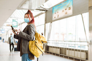 Young white woman wearing face mask using cellphone at train station