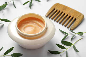 Jar of hair care cosmetic product, wooden comb and green leaves on white background, closeup