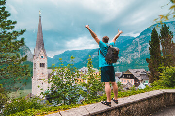 happy man tourist standing with rising up hands looking at hallstatt city from above