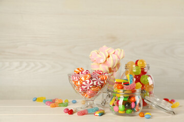 Jars with different delicious candies on beige wooden table, space for text