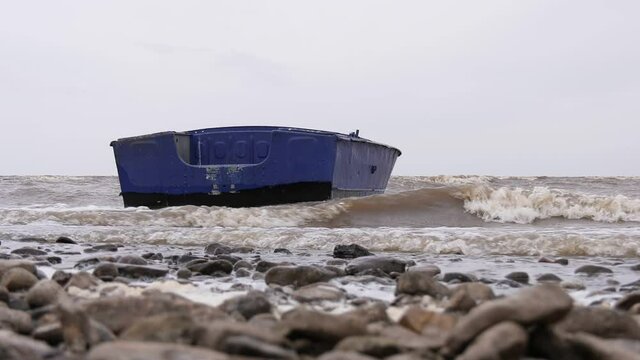 Blue metal boat swaying on the waves near the shore. Windy autumn weather on the shore of Lake Ilmen.