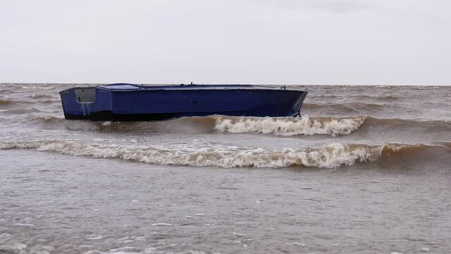 Blue metal boat swaying on the waves near the shore. Windy autumn weather on the shore of Lake Ilmen.