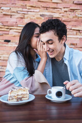 A young couple, smiling and happy, having fun and whispering, she whispers in his ear.