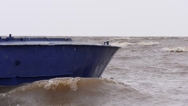 Blue metal boat swaying on the waves near the shore. Windy autumn weather on the shore of Lake Ilmen.