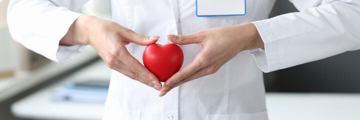 Doctor holding red toy heart in his hands in clinic closeup