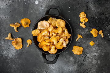 Chanterelle mushrooms, in cast iron frying pan, on black dark stone table background, top view flat lay - obrazy, fototapety, plakaty