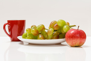 Bunch of green grapes, cup of coffee and apple on white background.