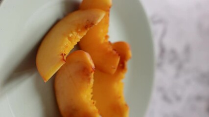 Pieces of fresh and aromatic ripe peach are on the plate. Side view, shallow depth of field. Close-up and selected focus. Vertical Video - Powered by Adobe