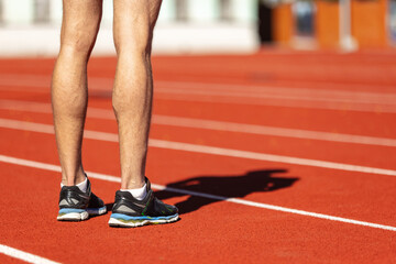 Cropped image of male athlete, runner training at public stadium, sport court or running track outdoors. Summer sport games. Man's legs