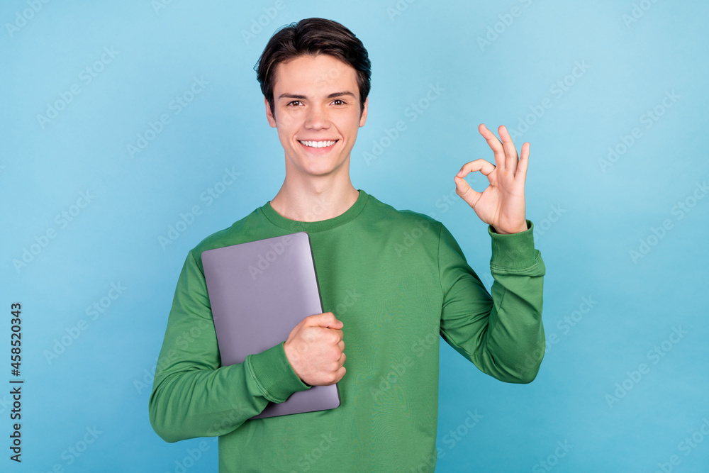 Wall mural Photo portrait young guy keeping laptop showing okay gesture smiling isolated pastel blue color background