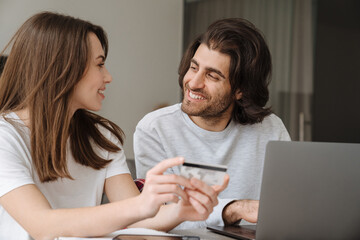 Young multiracial couple using credit card while working with laptop