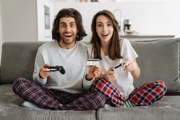 Young multiracial couple using credit card while playing online game