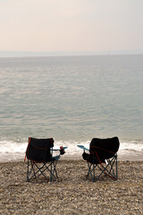 Fototapeta na wymiar Collapsible beach chairs on pebble stone beach