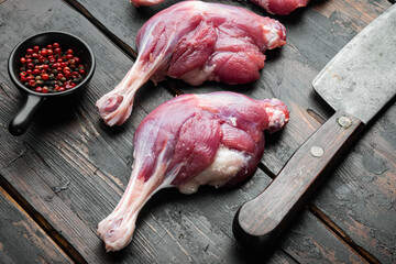 Raw goose legs thighs  with old butcher cleaver knife, on old dark  wooden table background