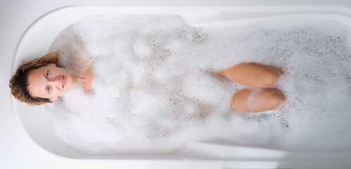 Young woman lying in warm bath with foam top view