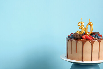 Chocolate birthday cake with berries, cookies and number thirty golden candles on blue wall...