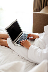 a man with a laptop on the bed. The man in the bedroom is lying on a bed with a computer on his lap and a notebook in his hands. A man works at home, writes in a notebook.