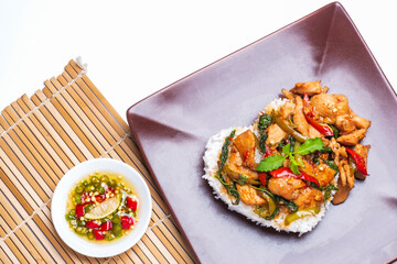 Stir fried chicken with basil over rice in a brown plate.
