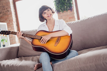 Full length body size photo young woman playing acoustic guitar sitting on sofa alone in apartment