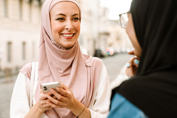 Multiracial muslim women wearing hijab talking while using mobile phone