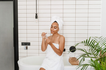 Young black woman wrapped in towels applying face serum